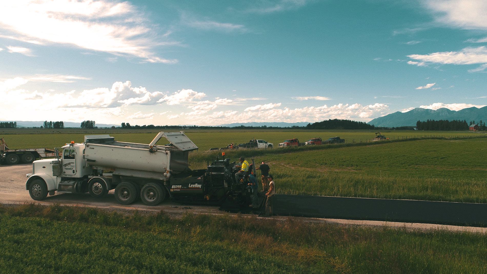 Treasure State Concrete, Inc. paving crew placing asphalt beside Montana farmland
